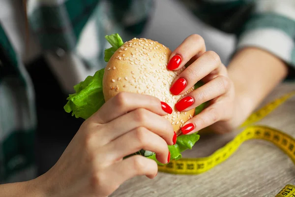 Mujer con hamburguesa y cinta métrica mientras hace dieta — Foto de Stock