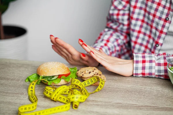 Женщина с бургером и измерительной лентой во время диеты — стоковое фото
