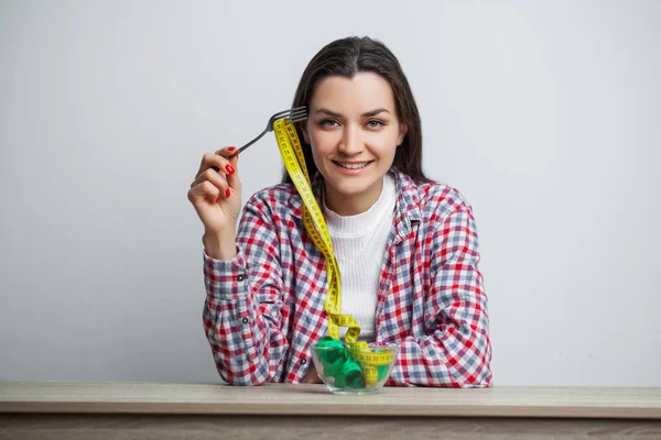 Young pretty woman adheres to diet with measuring tape on white wall background