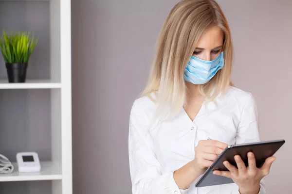 Woman doctor in protective mask working at tablet in office — Stock Photo, Image