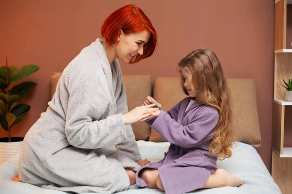 Mom makes daughter on the bed at home manicure