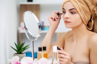 Kadın sabah makyajını evde banyo aynasında yapmaya hazırlanıyor.