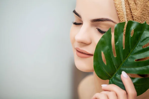 Vrolijke vrouw met een glimlach houdt een blad van een bloem in de buurt gezicht — Stockfoto