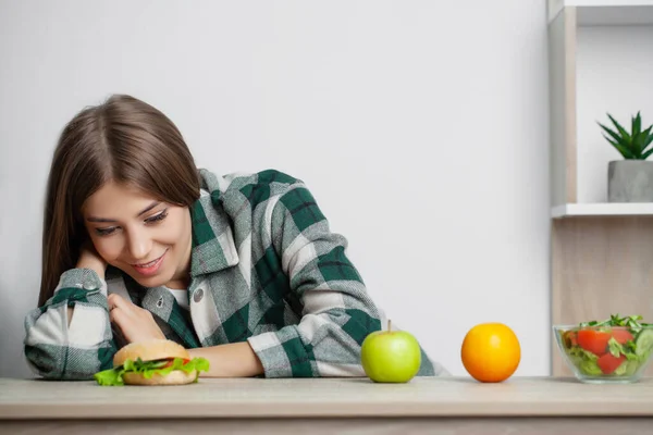 Mulher faz uma escolha entre alimentos saudáveis e prejudiciais — Fotografia de Stock