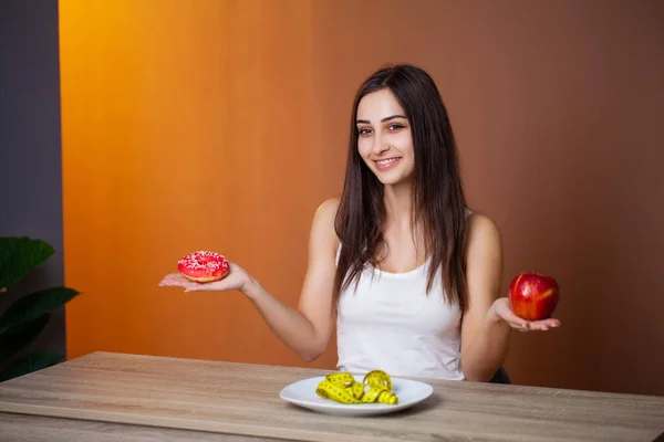 Retrato de una joven hermosa chica que hace una elección entre la comida saludable y perjudicial —  Fotos de Stock