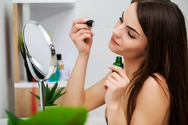 Cute girl puts makeup on the face in the bathroom