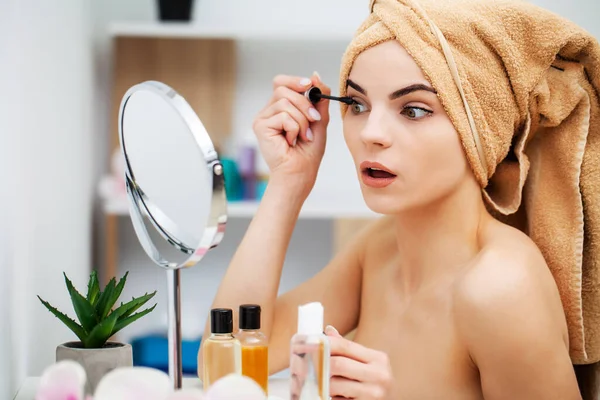 Cute girl puts makeup on the face in the bathroom