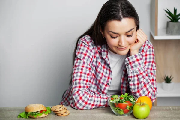 Menina faz uma escolha entre alimentos saudáveis e prejudiciais — Fotografia de Stock