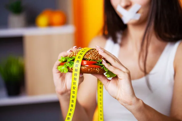 Концепция диеты женщина с запечатанным ртом держит жирный бургер — стоковое фото