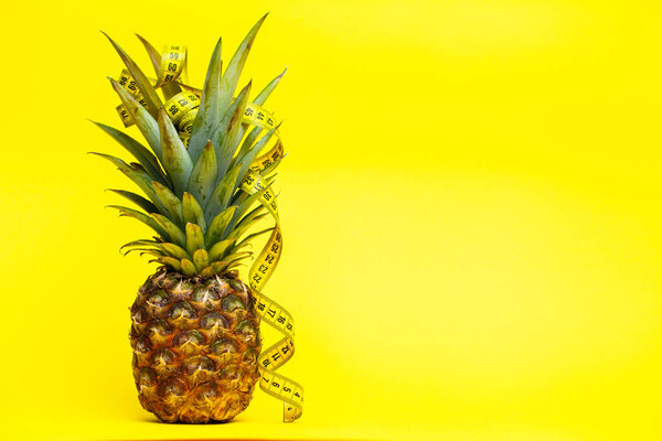 Ripe pineapple with tape measure on a yellow background