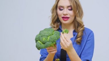 Masadaki bir kadın gri arka planda brokoli tutuyor.
