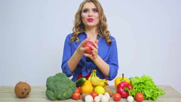Mujer en una mesa sosteniendo una manzana sobre un fondo de frutas y verduras — Vídeo de stock