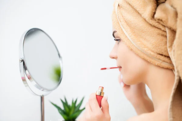 Pretty young woman puts makeup on the face in the bathroom