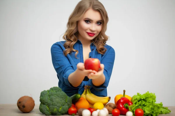 果物や野菜を背景にリンゴを持つテーブルの上でかわいい女性 — ストック写真