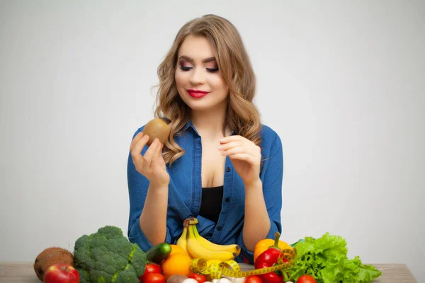Mujer linda en una mesa sosteniendo una manzana sobre un fondo de frutas y verduras — Foto de Stock
