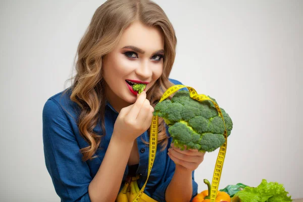 果物や野菜を背景にブロッコリーを持つテーブルでかわいい女性 — ストック写真
