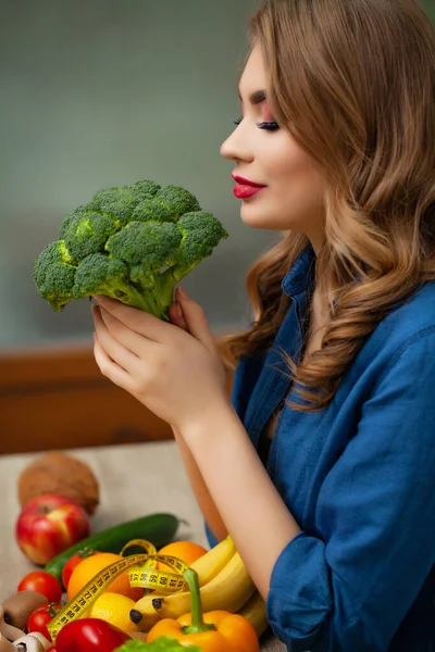 Mulher bonito em uma mesa segurando um brócolis em um fundo de frutas e legumes — Fotografia de Stock