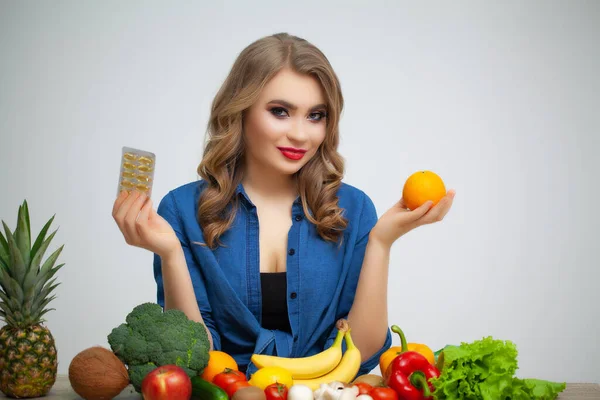 Bir masada elinde portakal ve meyve ve sebze arkaplanda haplar tutan bir kadın.. — Stok fotoğraf