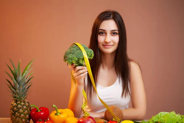 Aranyos nő egy asztalnál kezében brokkoli a háttérben a gyümölcs és zöldség — Stock Fotó