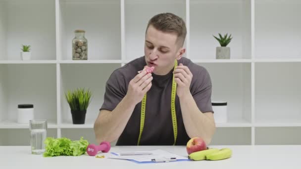 Mężczyzna sportowiec jedzenie pączka odrzucając w kierunku zdrowej żywności i odżywiania planu — Wideo stockowe
