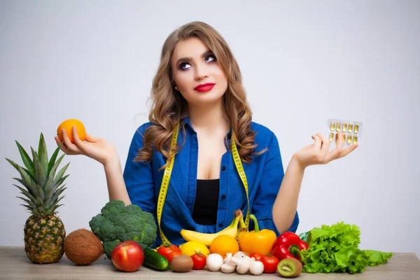 Жінка за столом тримає апельсин і таблетки на фоні фруктів і овочів — стокове фото