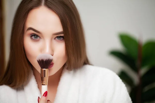 Cute young woman puts makeup on the face in the bathroom