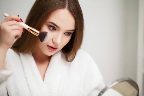 Linda joven mujer pone maquillaje en la cara en el baño — Foto de Stock