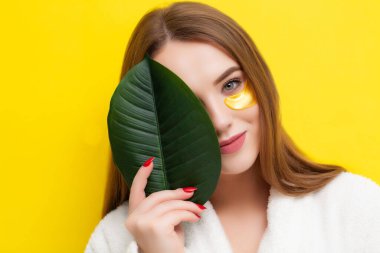 Güzel bir genç kadın sarı arka planda gözlerinin altına yamalar koyar.