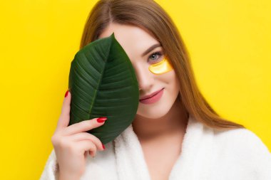 Güzel bir genç kadın sarı arka planda gözlerinin altına yamalar koyar.