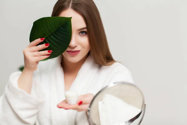 Hübsche junge Frau mit einer Creme zur Gesichtspflege im Badezimmer — Stockfoto