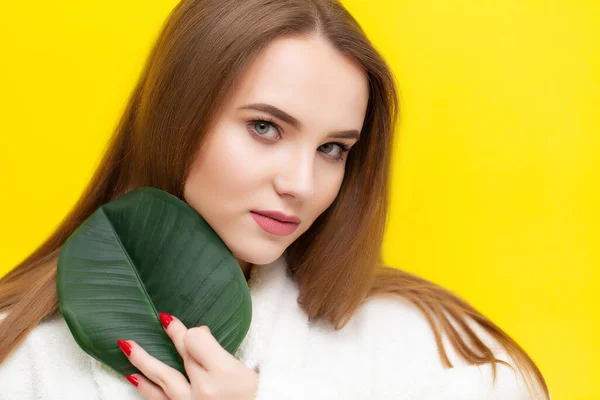 Όμορφο κορίτσι με μπουρνούζι και όμορφο δέρμα κρατώντας πράσινο φύλλο σε κίτρινο φόντο — Φωτογραφία Αρχείου