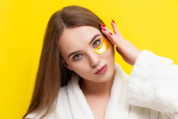 Όμορφη νεαρή γυναίκα βάζει μπαλώματα κάτω από τα μάτια σε ένα κίτρινο φόντο — Φωτογραφία Αρχείου