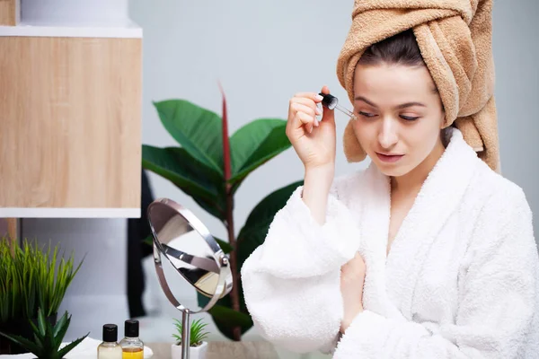 Mujer bastante joven pone maquillaje en la cara en el baño — Foto de Stock