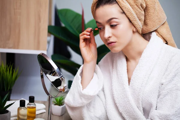 Mooie jonge vrouw zet make-up op het gezicht in de badkamer — Stockfoto