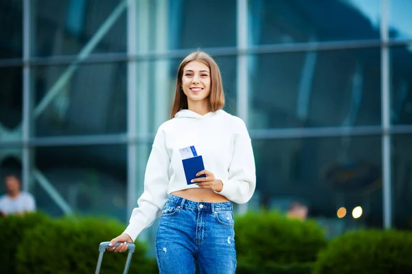 Eine Frau mit Pass und rotem Koffer in der Nähe des Flughafens ist unterwegs — Stockfoto