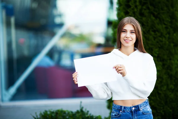 Hezká dívka v blízkosti letiště drží prázdný list papíru — Stock fotografie