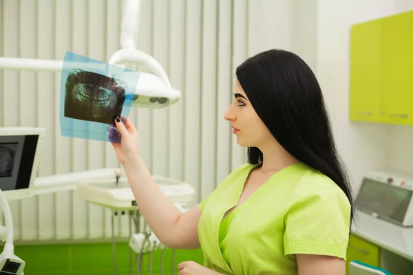 Молода жінка-лікар в зеленому пальто в стоматологічному кабінеті — стокове фото