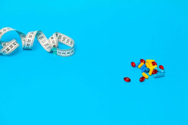 Pilules pour la perte de poids et ruban à mesurer sur fond bleu . — Photo