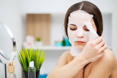 Bir kadın banyoda yüz bakımı maskesi kullanıyor.