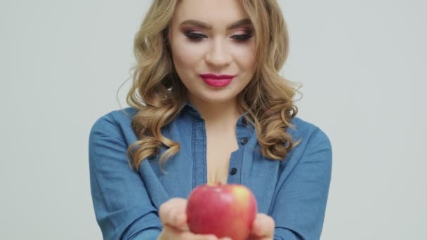 Nette Frau an einem Tisch mit einem Apfel auf einem Hintergrund aus Obst und Gemüse. — Stockvideo