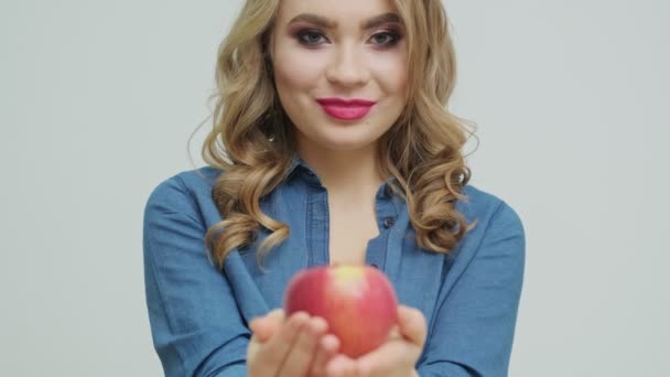 Милая женщина за столом держит яблоко на фоне фруктов и овощей . — стоковое видео