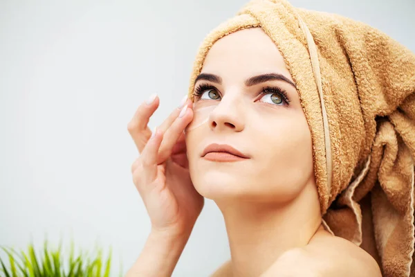 Pretty woman in a towel on her head applies patches on her face at home — Stock Photo, Image