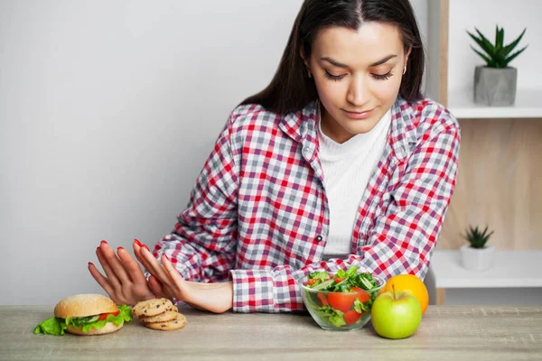 Mulher faz uma escolha entre alimentos saudáveis e prejudiciais . — Fotografia de Stock