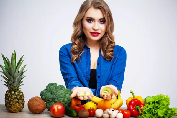 果物や野菜を背景にキウイと錠剤を持つテーブルの女性 — ストック写真