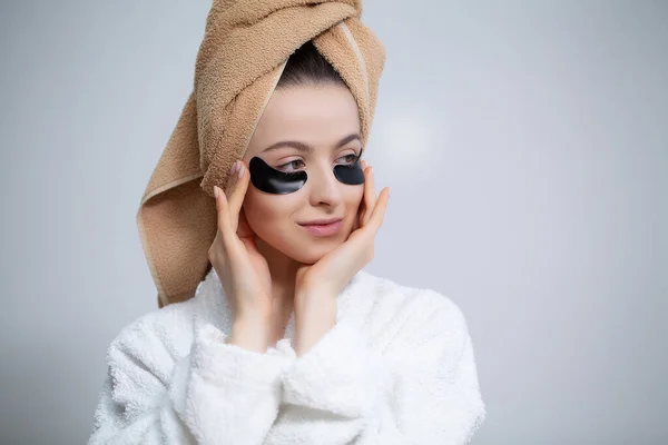 Hermosa mujer con un abrigo blanco aplica parches en los ojos para el cuidado de la piel — Foto de Stock