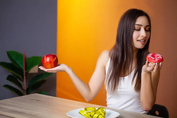 Mujer hermosa que hace una elección entre la comida útil y perjudicial —  Fotos de Stock