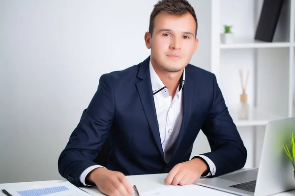 Joven trabajador guapo que trabaja en una oficina de la empresa con documentos y una computadora portátil —  Fotos de Stock