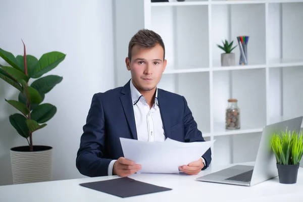 Stilig ung arbetare som arbetar på ett företag kontor med dokument och en bärbar dator — Stockfoto