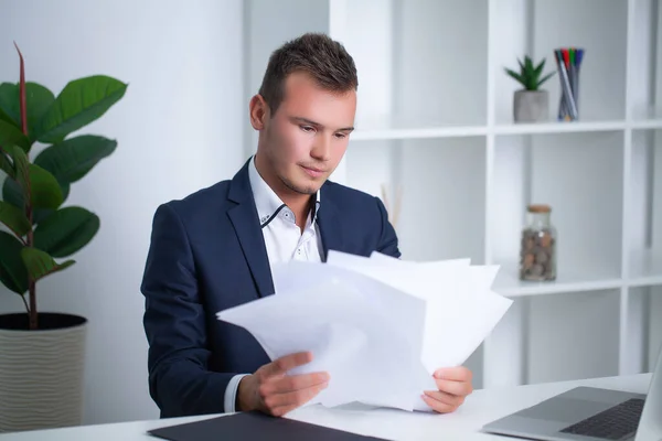 Handsome young worker working in a company office with documents and a laptop — Stock Photo, Image
