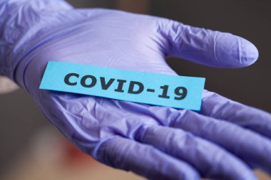 Koruyucu eldivenli bir kadın elinde Covid-19 yazısıyla.